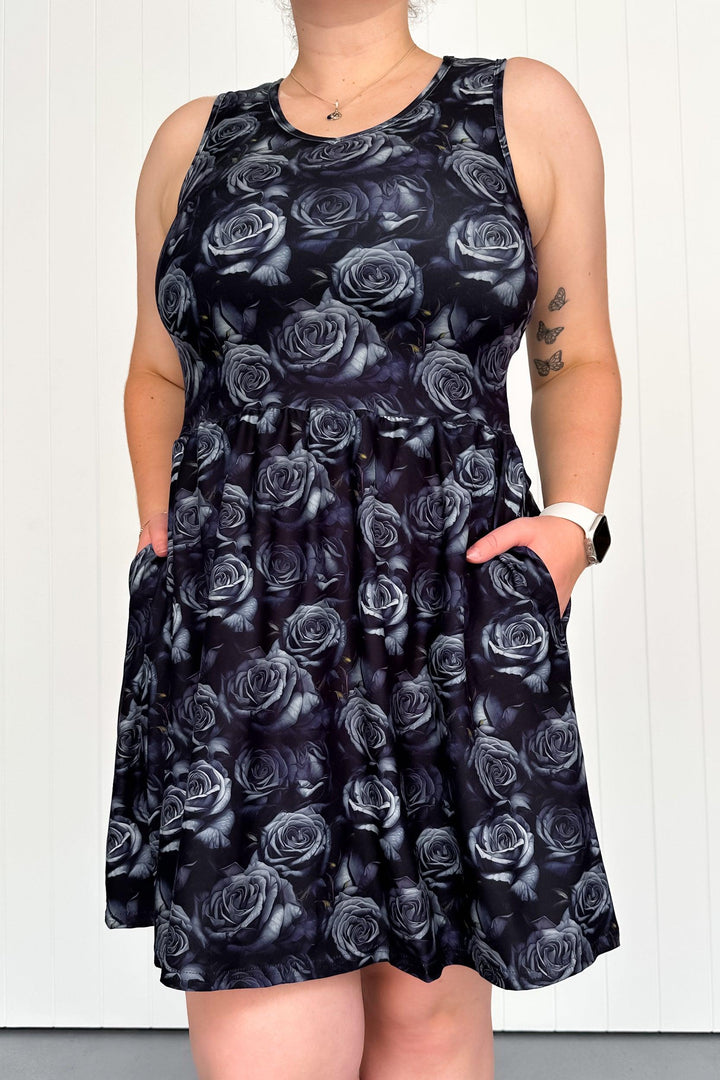 A sleeveless mini dress with a dark rose floral pattern and pockets, worn by a model.