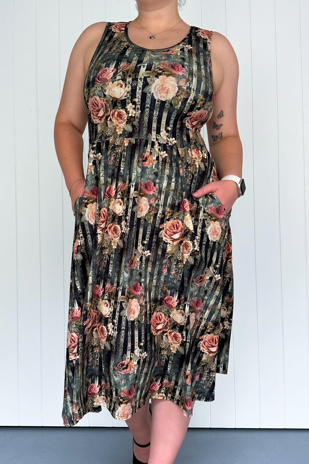 A sleeveless midi dress with a floral pattern in pinks and creams over dark vertical stripes, featuring a round neckline and deep side pockets.
