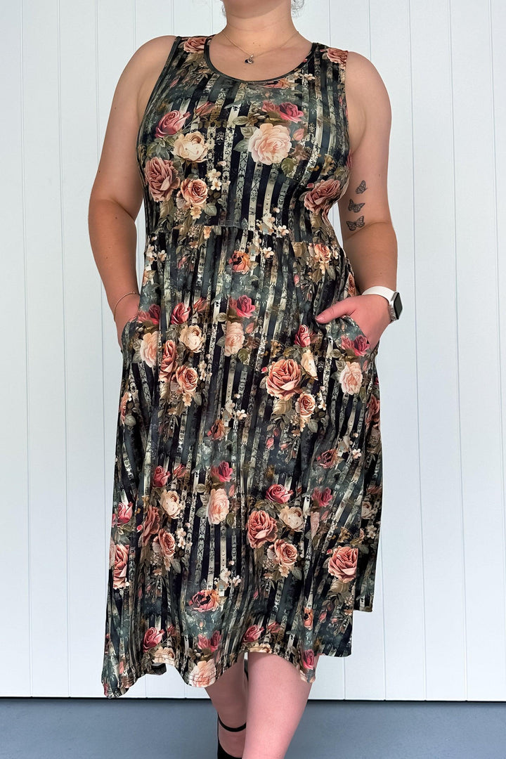 A sleeveless midi dress with a floral pattern in pinks and creams over dark vertical stripes, featuring a round neckline and deep side pockets.