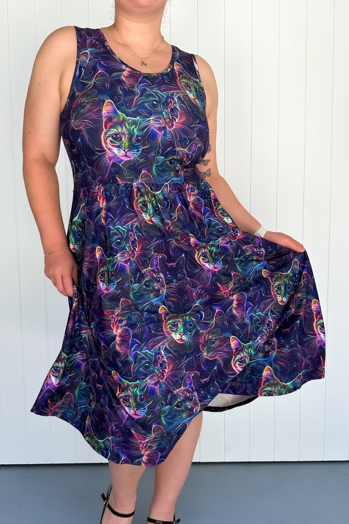 A sleeveless midi dress with a vibrant holographic cat print in neon purples, blues, greens, and pinks against a dark background, worn by a model.