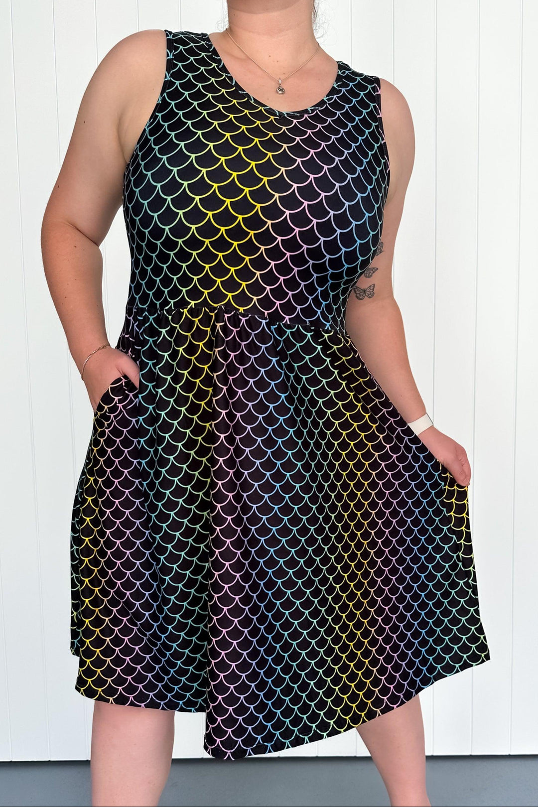Person wearing a sleeveless dress with a colorful fish-scale pattern against a white background
