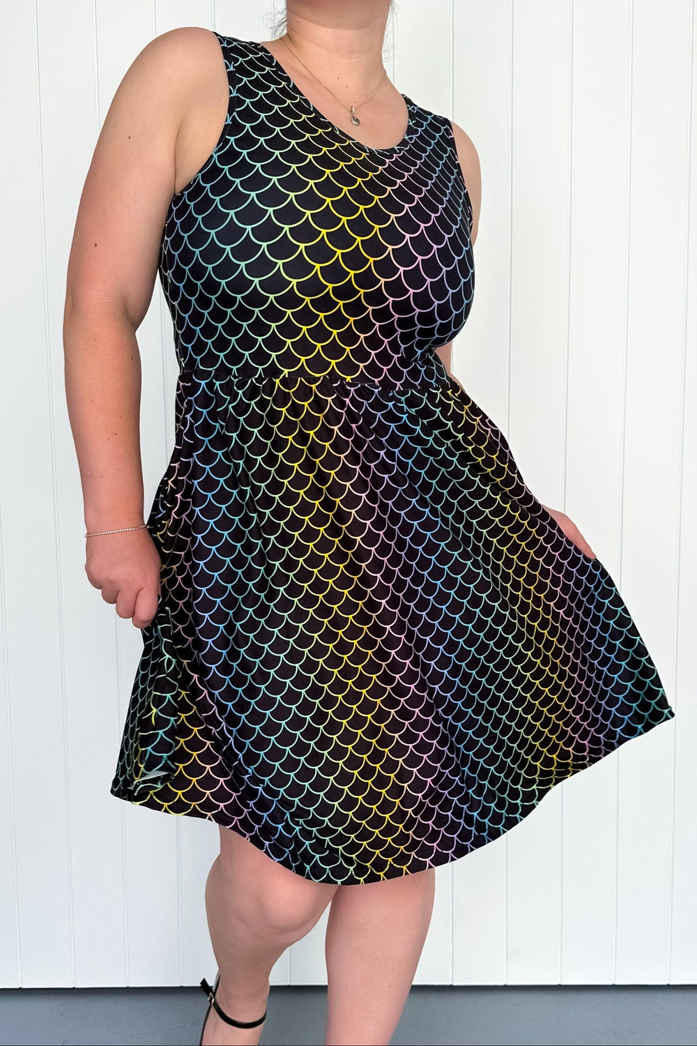 Person wearing a sleeveless dress with a colorful mermaid-scale pattern against a white background