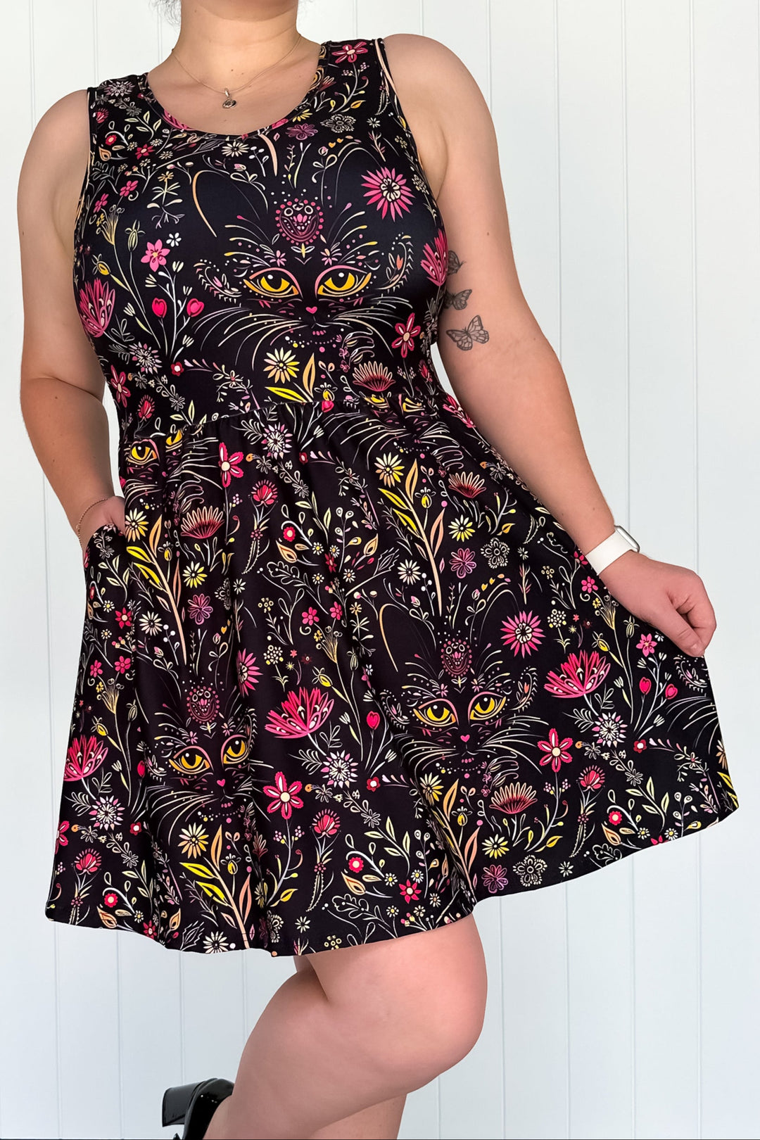 A sleeveless mini dress with a floral and cat face pattern, featuring side pockets.