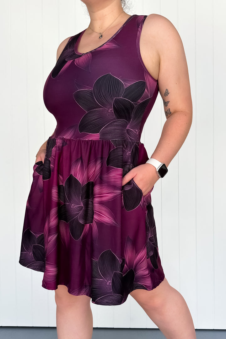 A person wearing a sleeveless mini dress with a floral pattern in shades of purple and black.