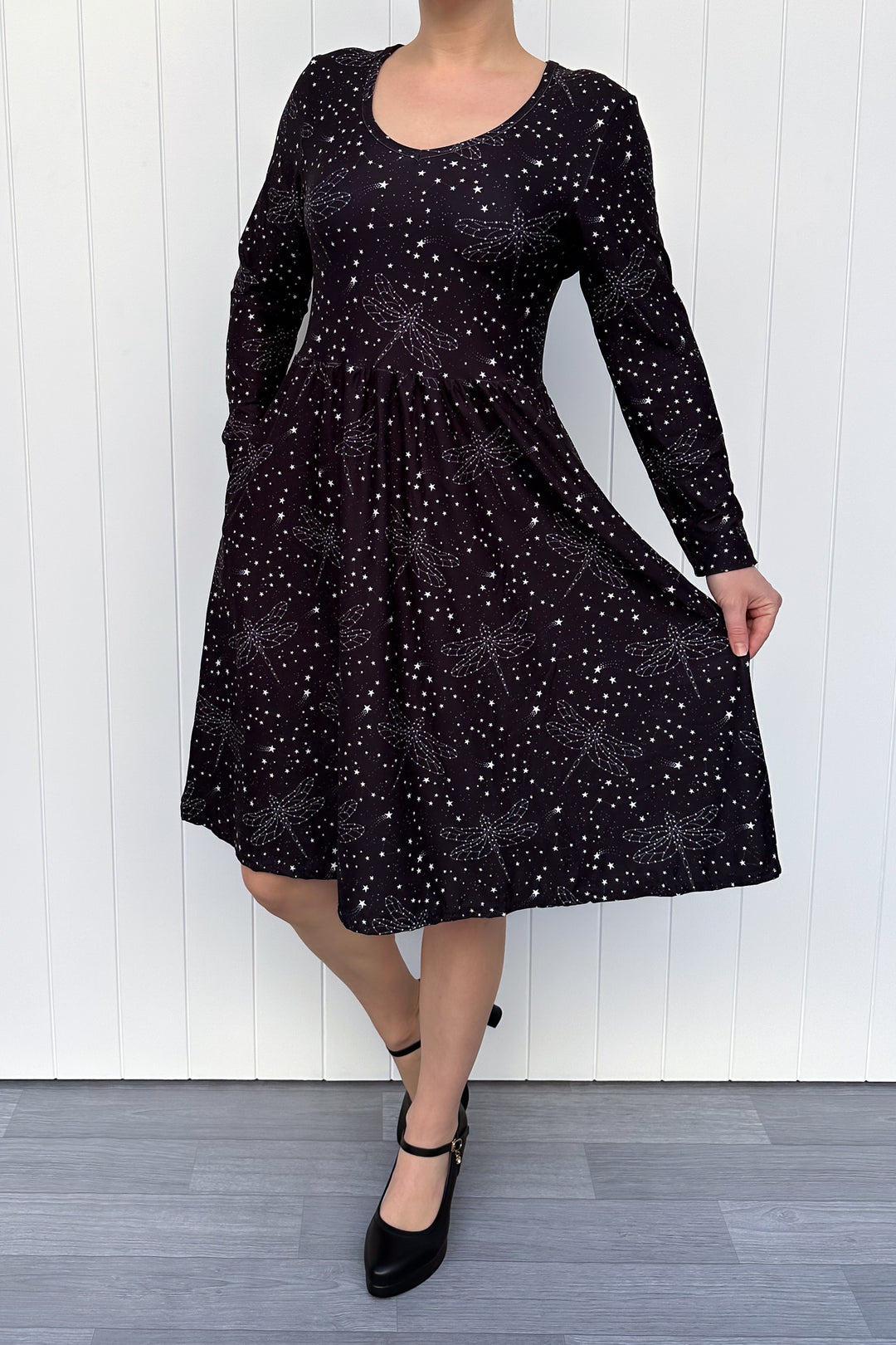 Person wearing a black dress with white dragonfly patterns against a white wooden panel background