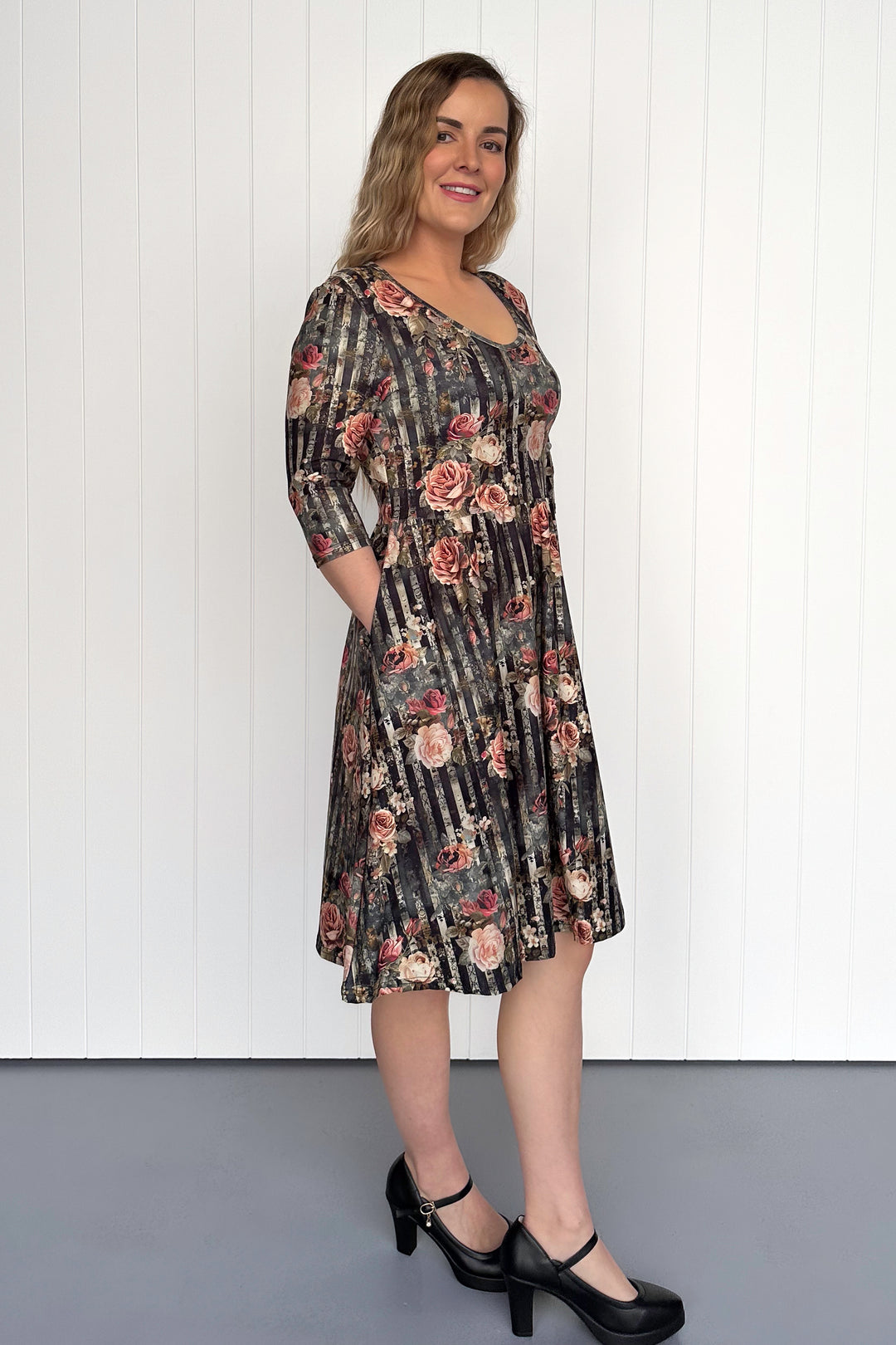 Woman wearing a floral dress standing against a white paneled wall.