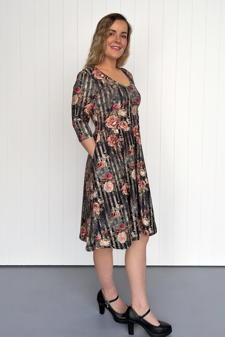 Woman wearing a floral dress standing against a white paneled wall.