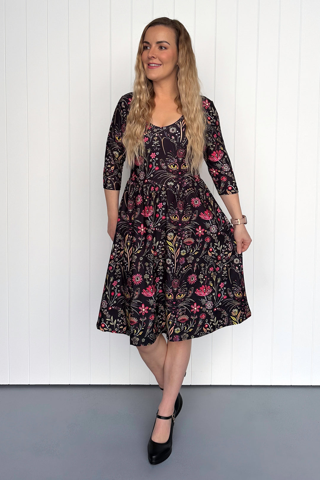 Woman wearing a floral cat dress against a white paneled wall.