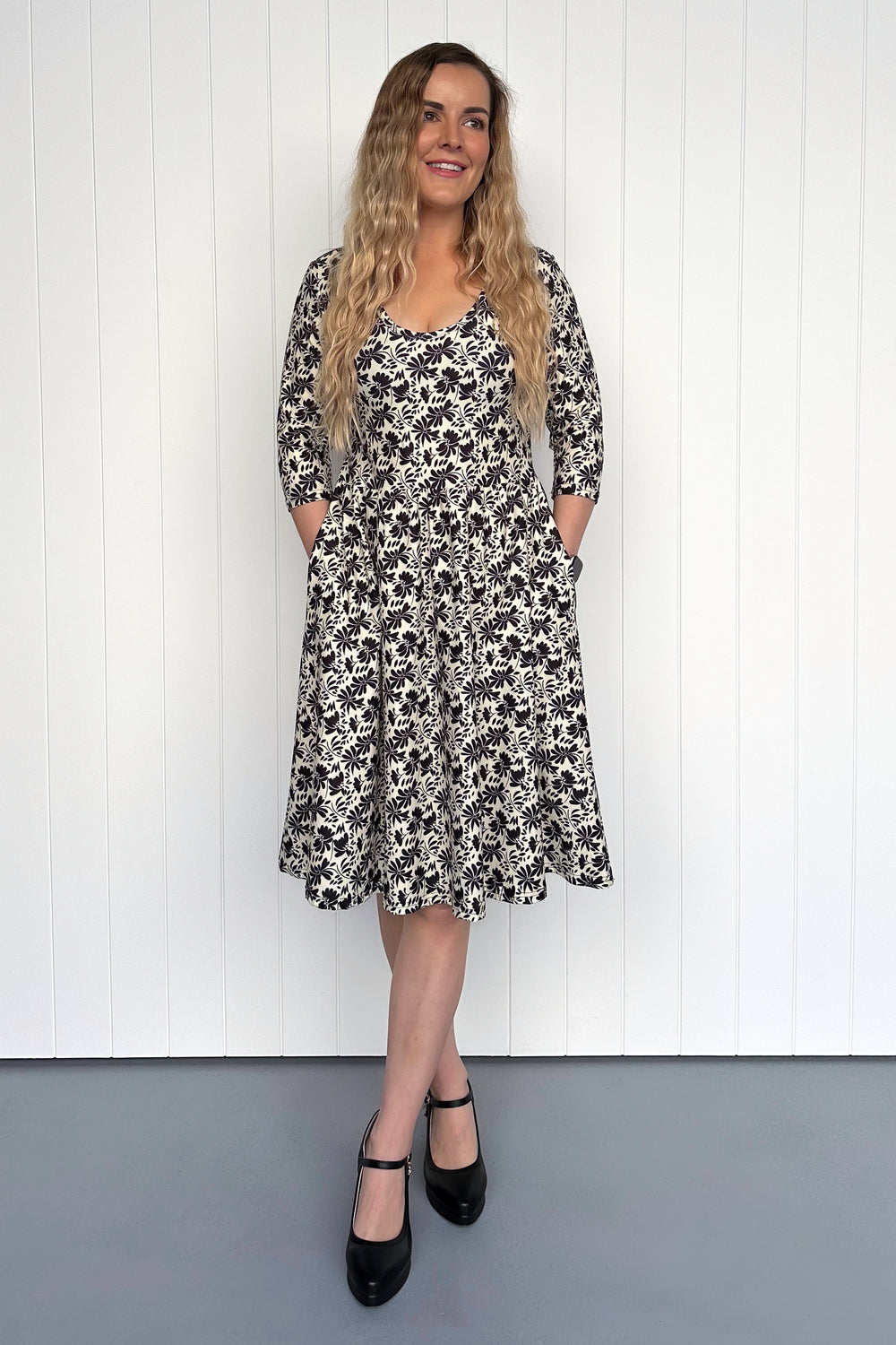 Woman wearing a black and white floral dress against a white wooden panel background