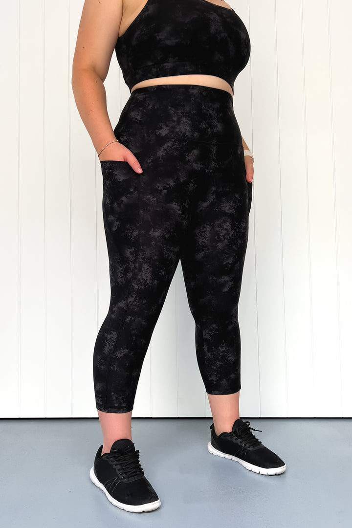 Person wearing black tie-dye leggings and crop top against a white background