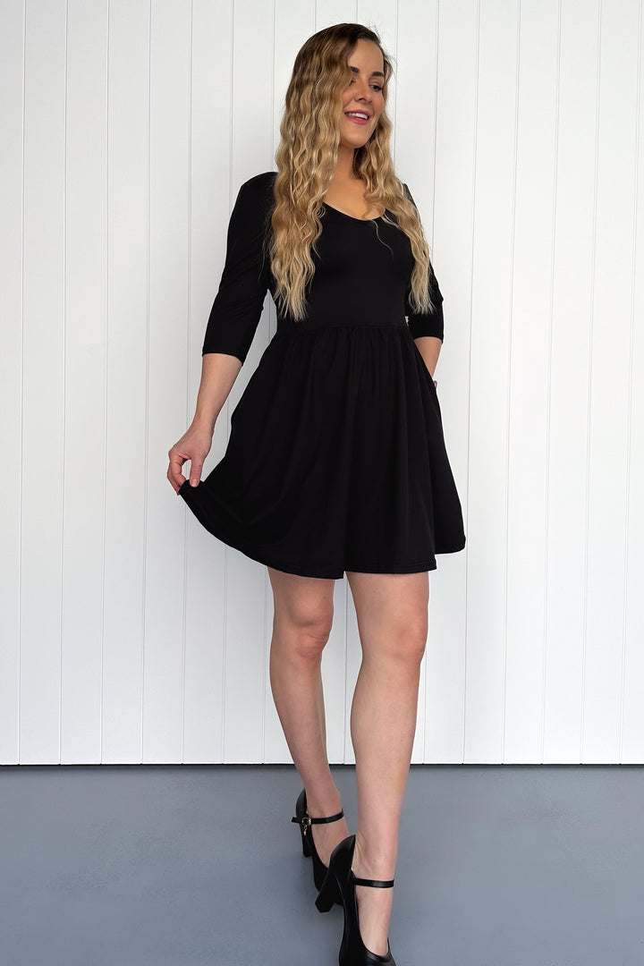 Woman wearing a black dress standing against a white wall.