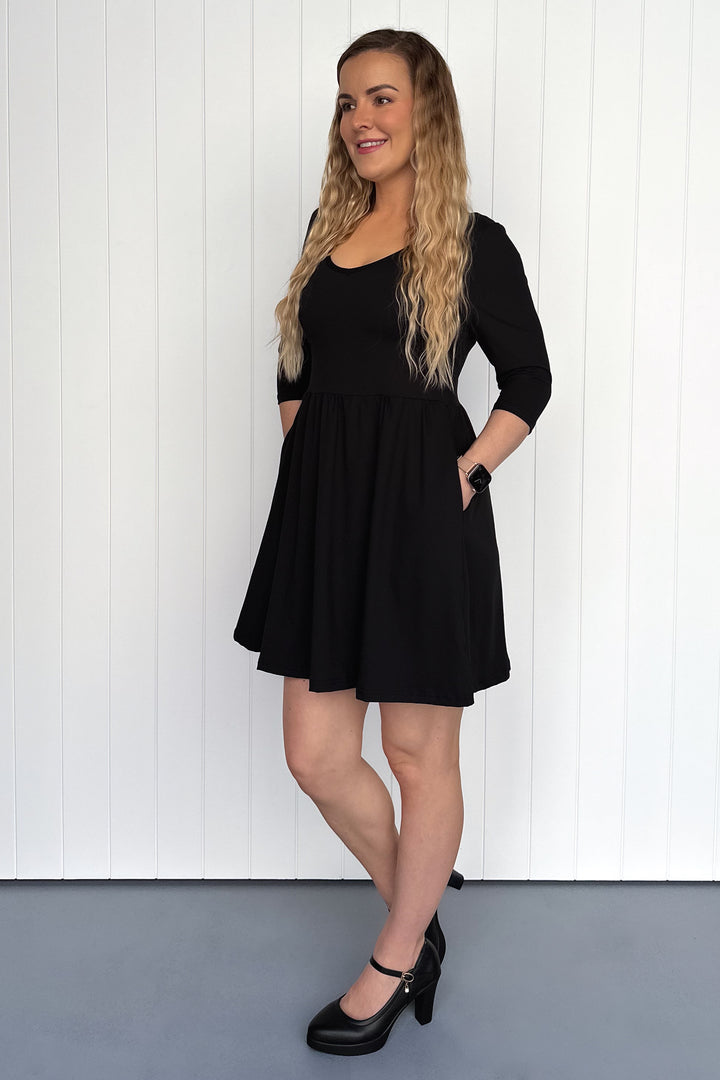 Woman wearing a black dress standing against a white wall.