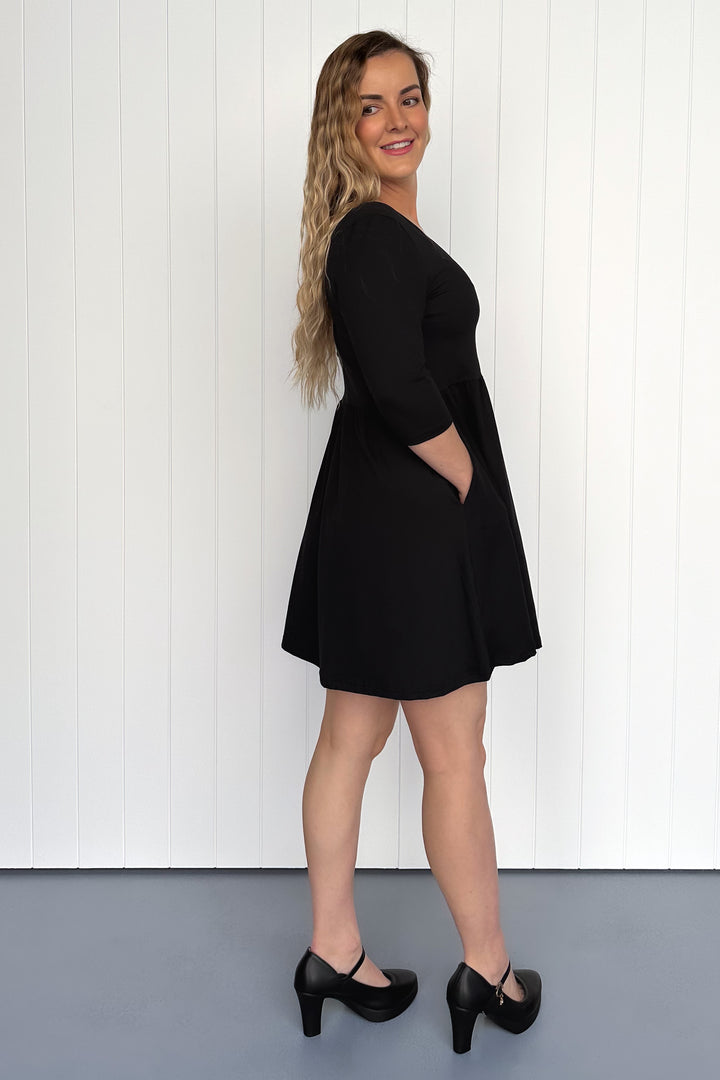 Woman wearing a black dress standing against a white wall.