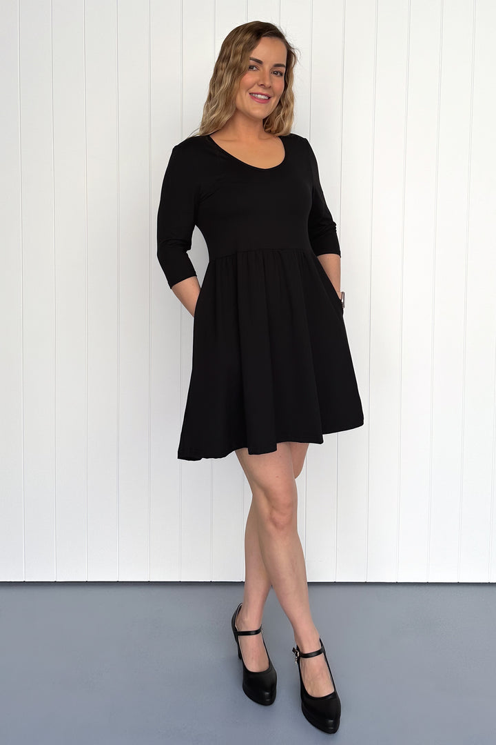 Woman wearing a black dress standing against a white wall.