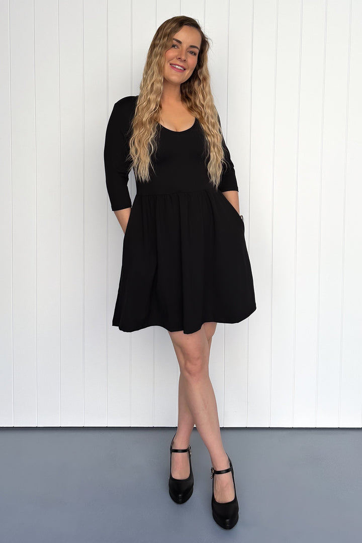 Woman wearing a black dress standing against a white wall.