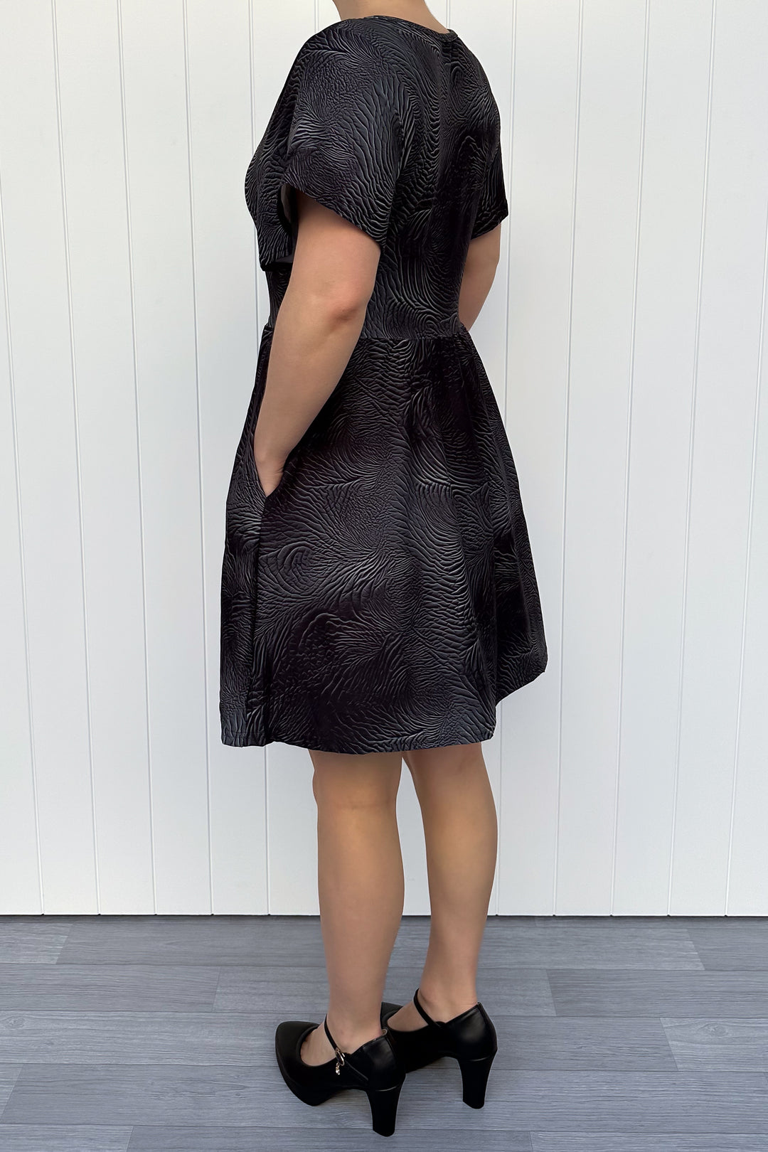 Person wearing a black leather patterned dress against a white wooden panel background