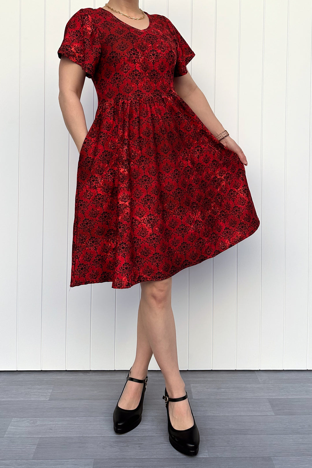 Person wearing a red floral dress against a white wooden panel background
