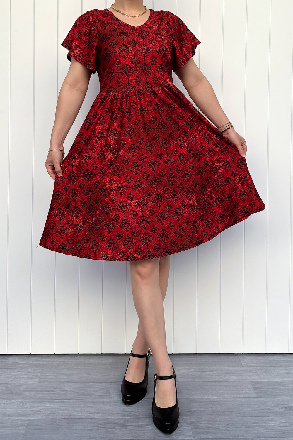 Red floral dress worn by a person against a white wooden panel background