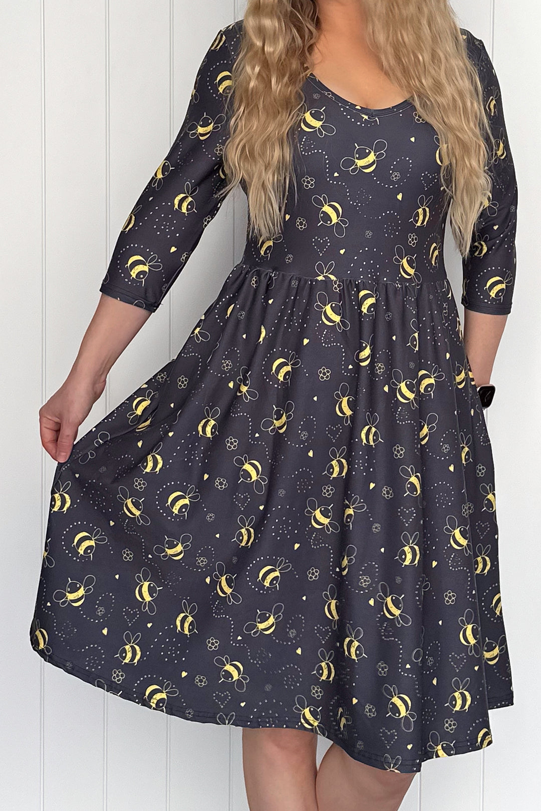 Woman wearing a dark grey dress with yellow bee pattern against a white wooden panel background
