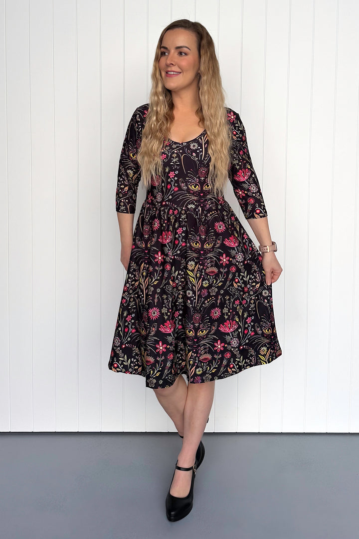 Woman wearing a floral cat dress against a white paneled wall.