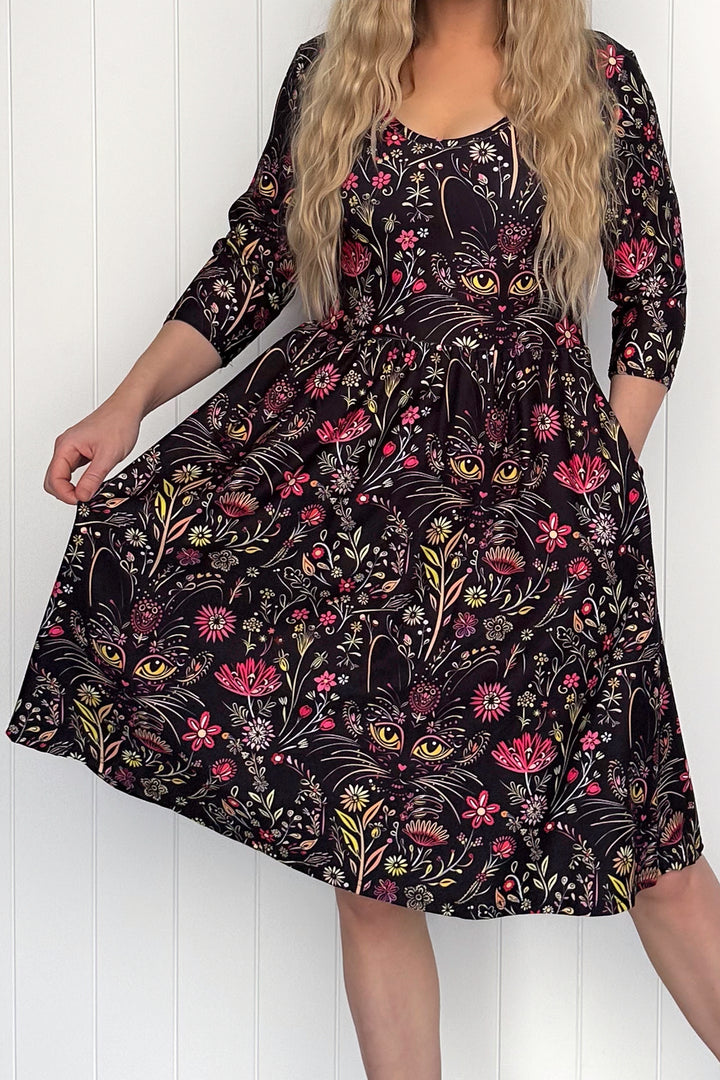 Person wearing a black dress with cat and floral pattern against a white wooden panel background