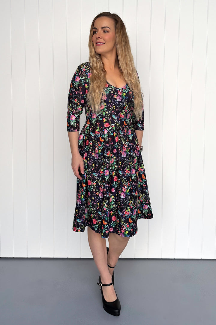 Woman wearing a floral bird dress against a white paneled wall.