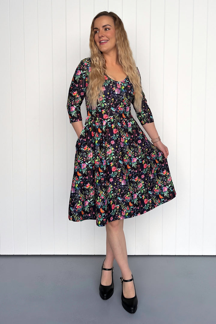 Woman wearing a floral bird dress against a white paneled wall.
